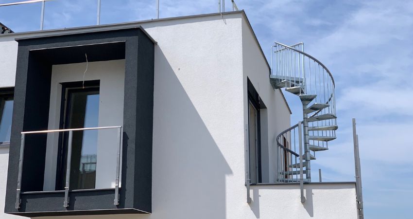 TORONTO vanjsko stubište – kompaktan dizajn za siguran pristup gornjoj etaži metalno spiralno stubište TORONTO montirano na vanjski balkon bijele suvremene kuće s ravnim krovom