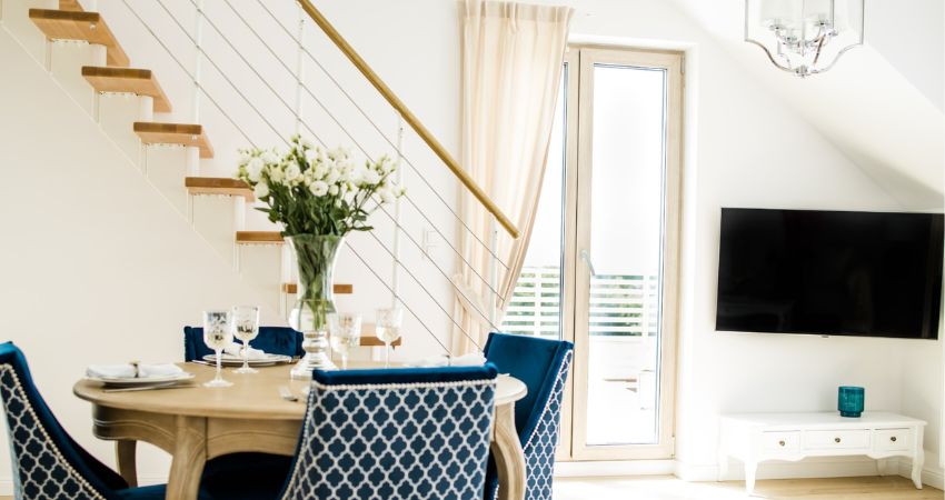 Stubište kao dekoracija – savršen spoj funkcije i stila u interijeru unutarnje stubište s drvenim gazištima i čeličnim sajlama uz blagovaonski stol i plave tapecirane stolice u svijetlom dnevnom boravku