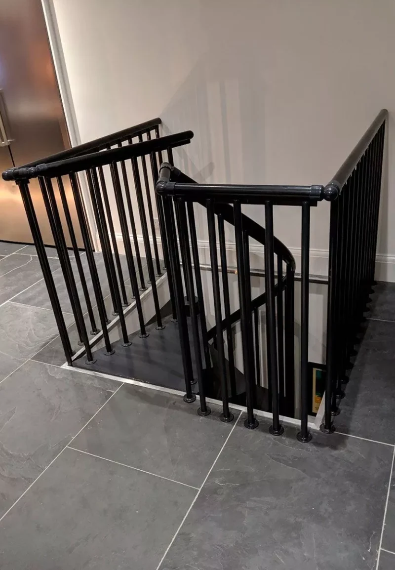 spiralno stubište MONTREAL s klasičnom ogradom u antracitnoj boji postavljeno na tamnim pločicama uz svijetli zid