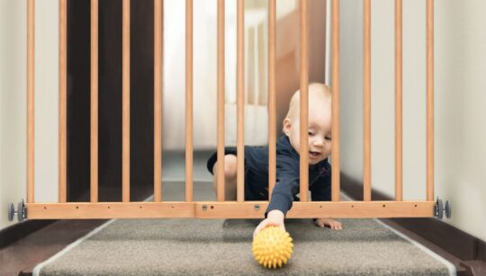 beba pruža ruku kroz drvenu zaštitnu pregradu kako bi dosegla žutu lopticu