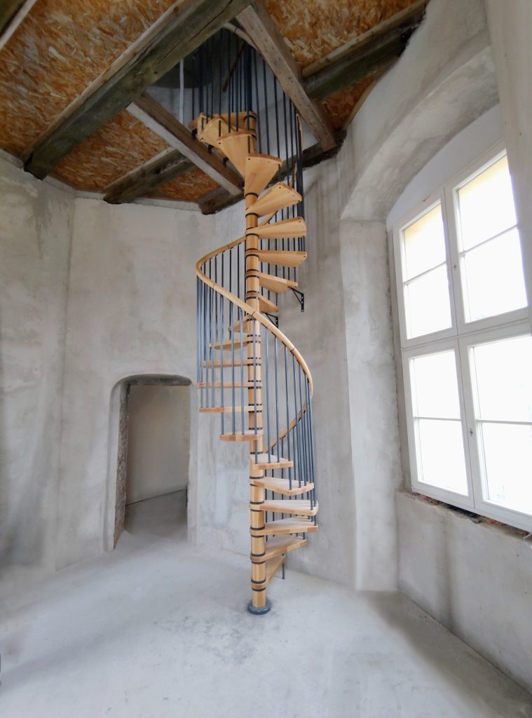 Kompaktne spiralne stepenice s drvenim gazištima u svijetlom povijesnom interijeru
