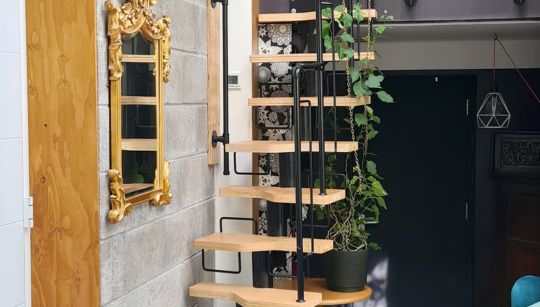 Modularne stepenice sa svijetlim drvenim gazištima koje vode na galeriju u eklektičnom interijeru.