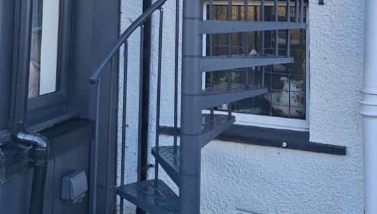 Antracitno spiralno stubište DOLLE TORONTO Ø125 s podestom postavljeno uz dograđeni zimski vrt